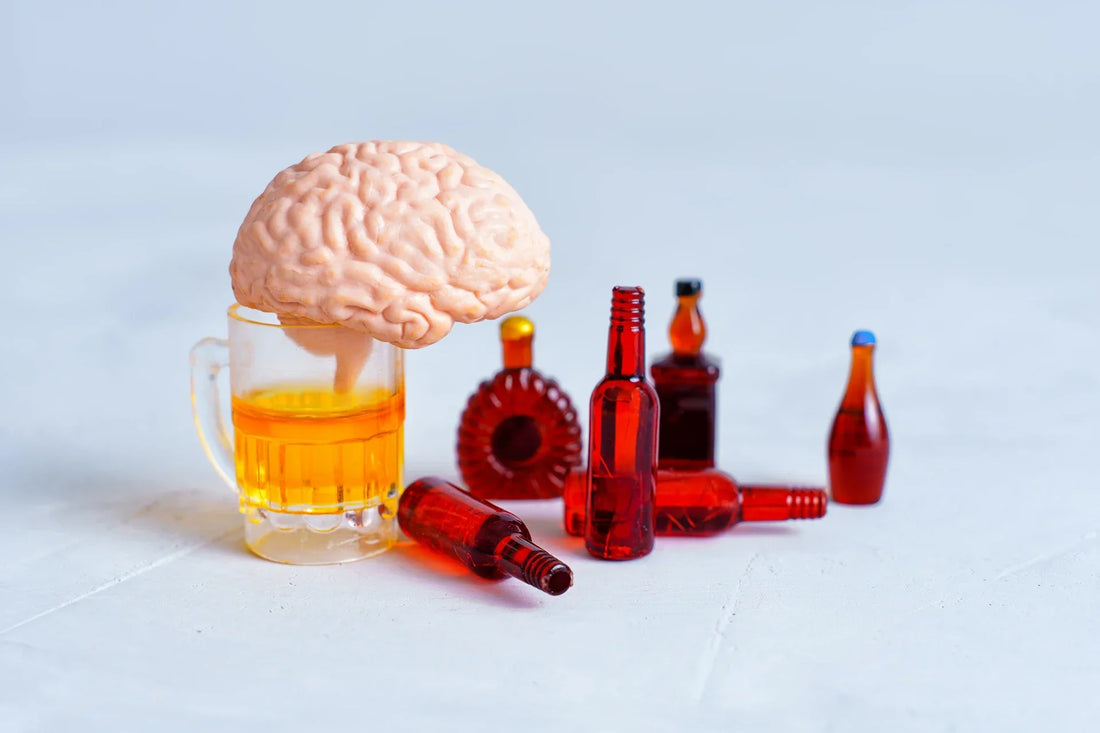 A plastic brain placed on a glass of alcohol, surrounded by miniature liquor bottles, symbolizing the impact of alcohol on brain function.