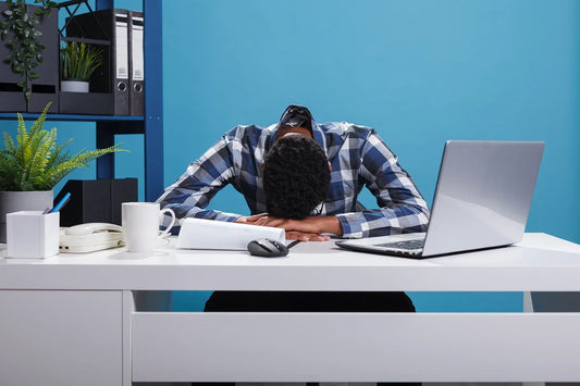 Exhausted man with his head down on a desk beside a laptop, symbolizing burnout, chronic stress, and its negative effects on brain health and cognitive function.