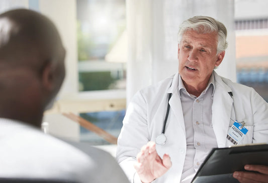 A senior doctor in a white coat having a serious conversation with a male patient during a consultation, emphasizing the importance of early evaluation for neurodegenerative diseases like Alzheimer’s and Parkinson’s.