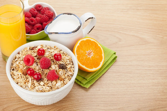 A healthy breakfast including a bowl of oats with berries, orange juice, milk, and fresh fruit on a wooden table, representing brain-friendly nutrition.