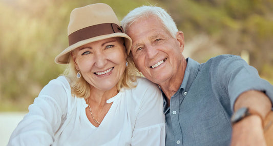 Smiling senior couple sitting outdoors, representing men and women affected by neurodegenerative diseases.