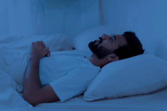 Man lying awake in bed at night, appearing sleep-deprived and restless